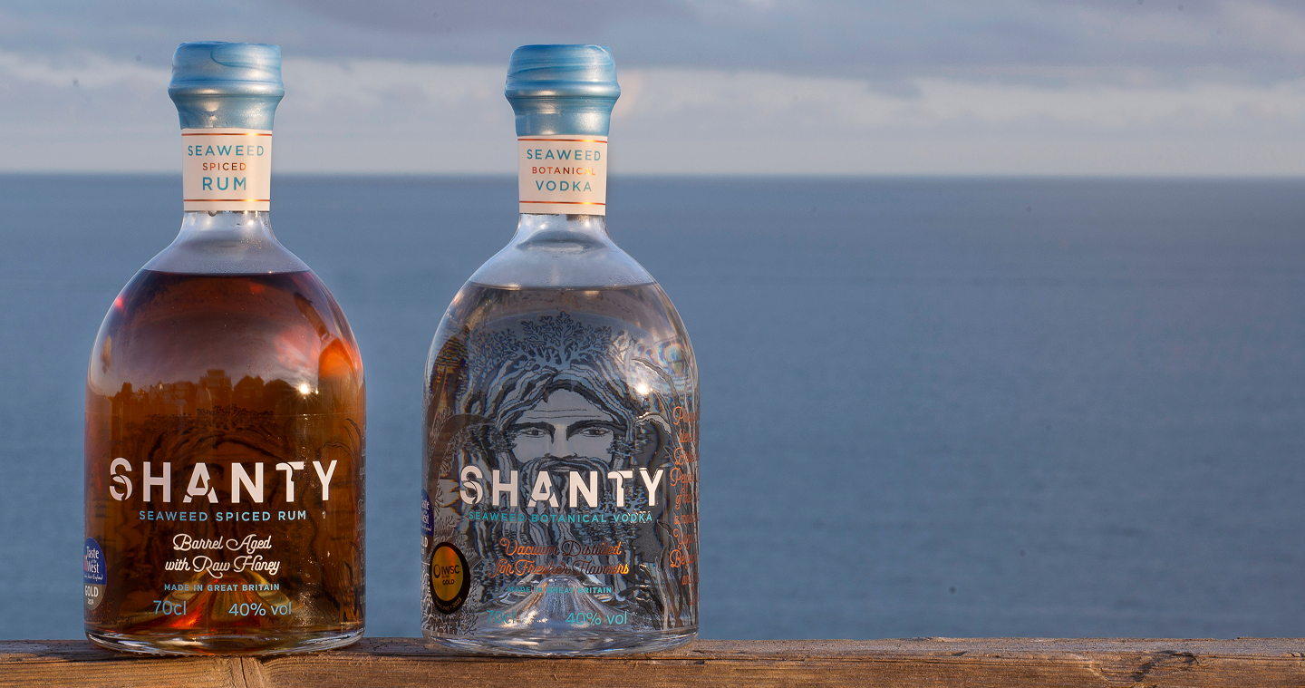 Two bottles of Shanty rum and vodka on a wooden surface with a blue sky background