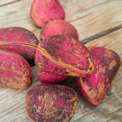 Handful of reddish-pink kola nuts piled on weathered pale wooden boards