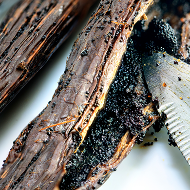 Close-up of split vanilla pods with a knife scraping out tiny black vanilla seeds